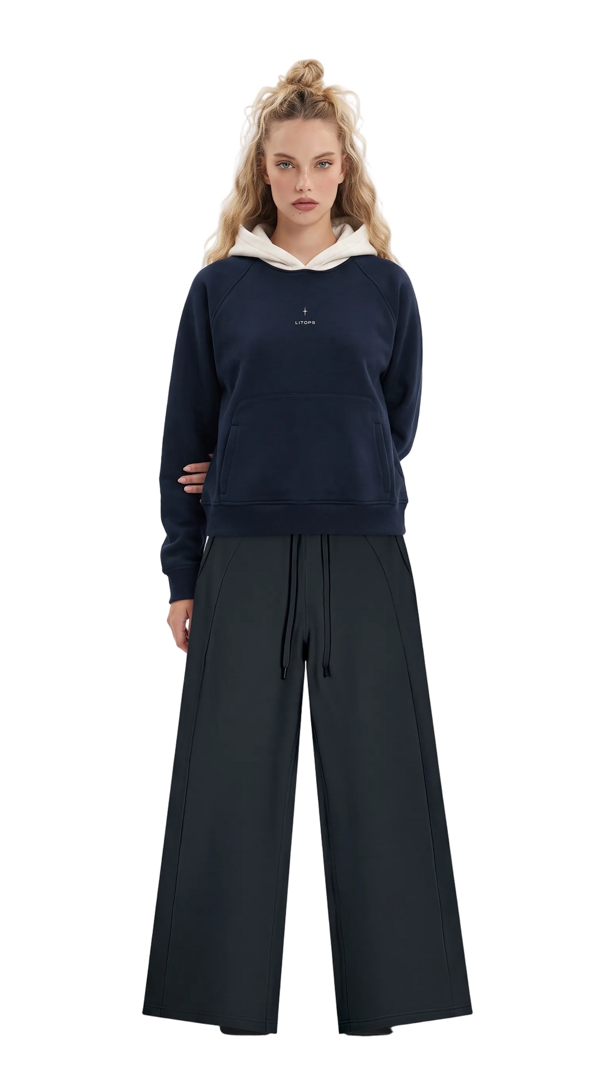 A model stands against a plain white studio background wearing a navy blue hoodie with a contrasting cream hood and a small white chest logo, paired with wide-leg black pants.